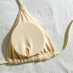 Detailed close-up of beige triangle bikini cup with lace trim and ribbed texture fabric