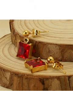 Detail of 18K gold-plated square red zircon earrings on natural wood stand