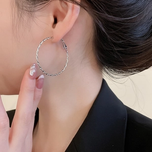 Détail macro de boucles d'oreilles créoles torsadées argentées au fini métallique brillant