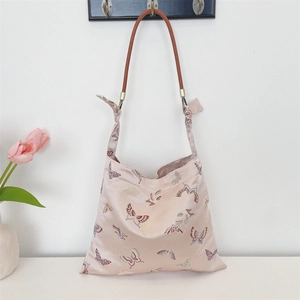 Close-up of pink satin shoulder bag with butterfly embroidery and woven leather handle