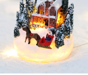 Detail of glowing resin Christmas village house with horse-drawn sleigh and snowy trees