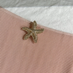 Close-up of golden starfish charm with granular texture on pink mesh fabric