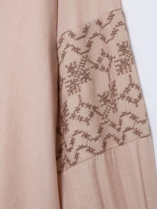 Close-up of intricate dark embroidery on light beige vintage V-neck long sleeve shirt fabric