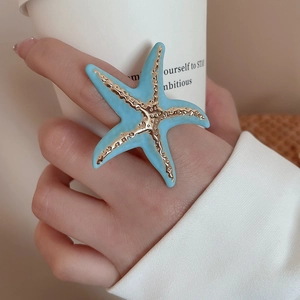 Detail of blue enamel starfish ring with gold accents on model's hand with coffee