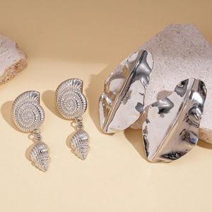 Silver shell conch and abstract leaf stud earrings shown on minimalist stone props