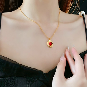 Detailed view of a vintage gold oval necklace with a red gemstone on a model's neck