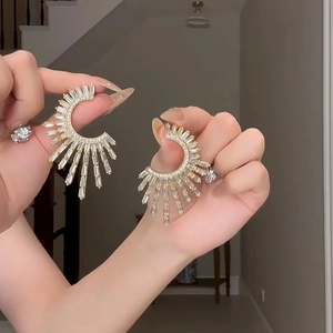 Detail of fan-shaped golden earrings with rectangular zircons held by hand model
