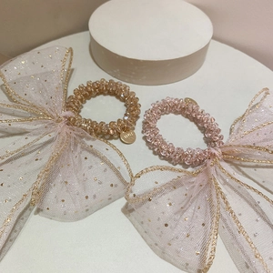 Detail of pink and gold beaded hair ties with sequined mesh bows on white stage