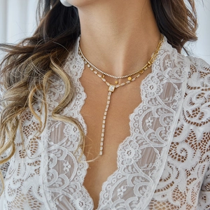Close-up of a double-layered 18k gold Y-necklace with zircon stars on white lace top