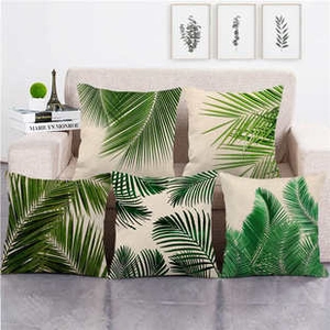 Set of five square throw pillow covers with green palm leaf patterns on a beige sofa