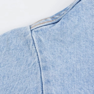 Detail of light blue washed denim short jumpsuit with yellow double stitching craftsmanship
