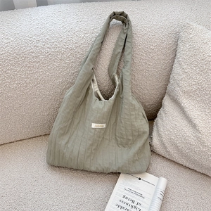 Detail of sage green pleated fabric tote bag resting on a cream bouclé textured sofa