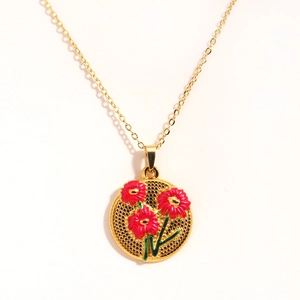 Vue macro d'un pendentif doré avec tulipes rouges et feuilles vertes sur un fond texturé quadrillé