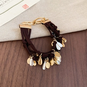Detailed view of layered fabric cord bracelet with gold and silver teardrop pendants