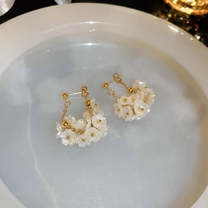 Detail von eleganten Goldohrringen mit weißen Blumenanhängern und langen Kettenfransen