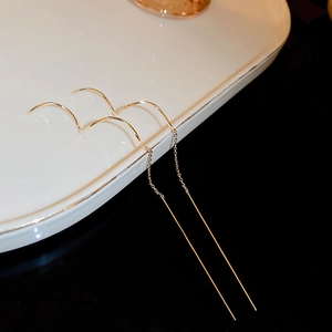Detail view of golden tassel chain earrings on a white ceramic tray with high contrast