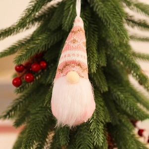 Close-up of a pink and white knitted Christmas gnome hanging on a festive tree branch