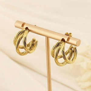 Golden twisted C-shaped hoop earrings displayed on a minimalist gold jewelry stand