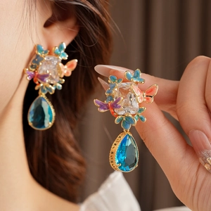 Detail of vintage gold drop earrings with colorful enamel butterfly and blue crystal