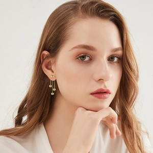 Elegant gold ball tassel earrings with a glossy metallic finish on a female model