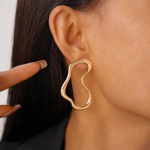 Close-up of a model wearing large irregular gold wavy hoop earrings with metallic shine