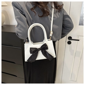 Detail view of white crossbody bag with black satin bow worn by a model in a home setting