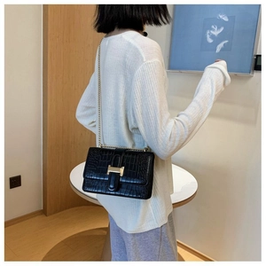 Detail of black crocodile texture shoulder bag with golden H buckle and chain strap on model