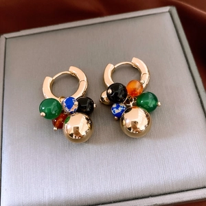 Détail macro de créoles dorées avec perles de pierre multicolores et sphère dorée polie