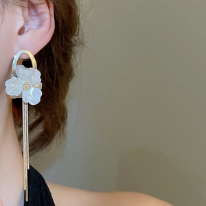 Detail of elegant white flower earrings with long gold tassel chains on model