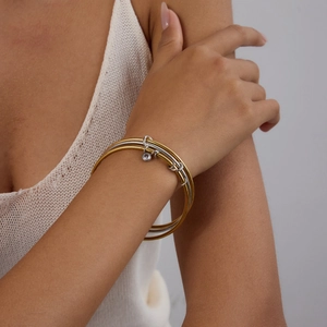 Three-piece layered 18k gold and silver bangle set with a single diamond pendant charm