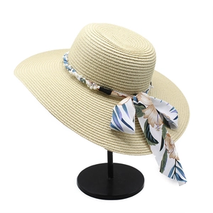 Detail of beige straw hat with floral ribbon, white pearls, and foldable wide brim