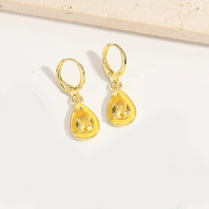 Close-up of elegant gold teardrop earrings with bright yellow zircon stones on white stone