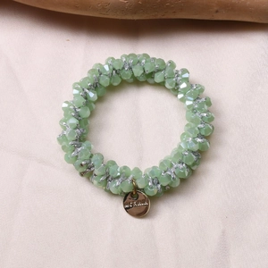 Close-up of light green beaded hair tie with gold brand tag on silk background