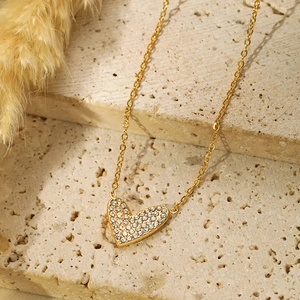 Macro shot of gold-plated heart necklace with micro-paved zircons on a textured stone surface