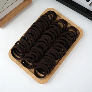 Detailed view of dark brown elastic seamless hair ties arranged in a wooden tray