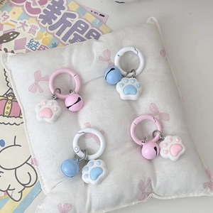 Cute cat paw bell keychains in pink and blue colors on a soft white decorative pillow