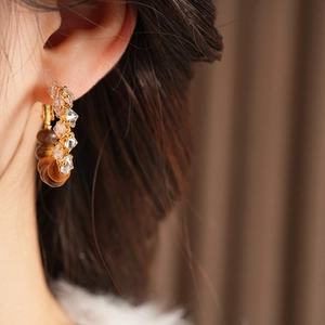 Close-up of golden hoop earrings with tiger eye stone and crystals on a model