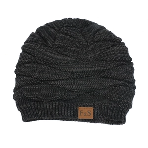 Close-up of thick cable knit texture and leather brand patch on dark gray beanie