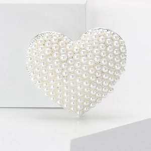 Detailed close-up of heart-shaped brooch with pearls on white geometric pedestals