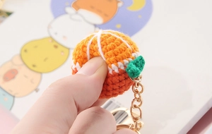 Close-up of handmade knitted orange pendant with green leaf and golden metal keychain