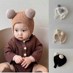 Detail showing knit baby earflap hats with pom-poms in coffee, white, beige, and black