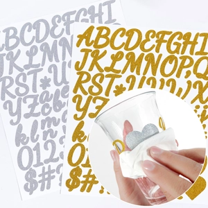 Macro detail of gold and silver glitter alphabet stickers applied to a glass cup surface