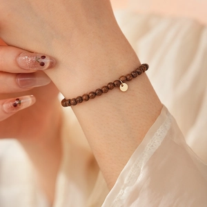 Close-up of agarwood beaded bracelet with a gold charm on a woman's wrist