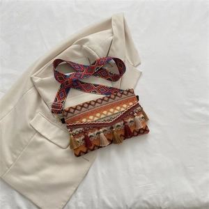 Close-up of geometric embroidery and colorful tassel charms on a woven crossbody bag