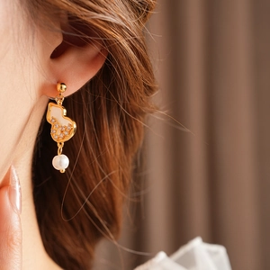 Close-up of gold gourd earrings with sparkling zircon, shell inlay and white pearl drops