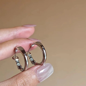 Sleek silver hoop earrings with polished mirror finish held against a warm brown background