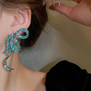 Macro shot of oversized bow earrings with turquoise rhinestones on model's ear