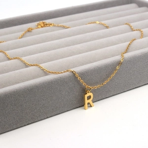 Detailed macro view of a gold-plated letter R pendant necklace in a soft velvet jewelry box