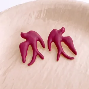 Elegant deep maroon bird-shaped stud earrings with gold edges on beige ceramic dish
