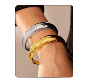 Close-up of thick polished C-shaped metal bracelets in gold and silver finish